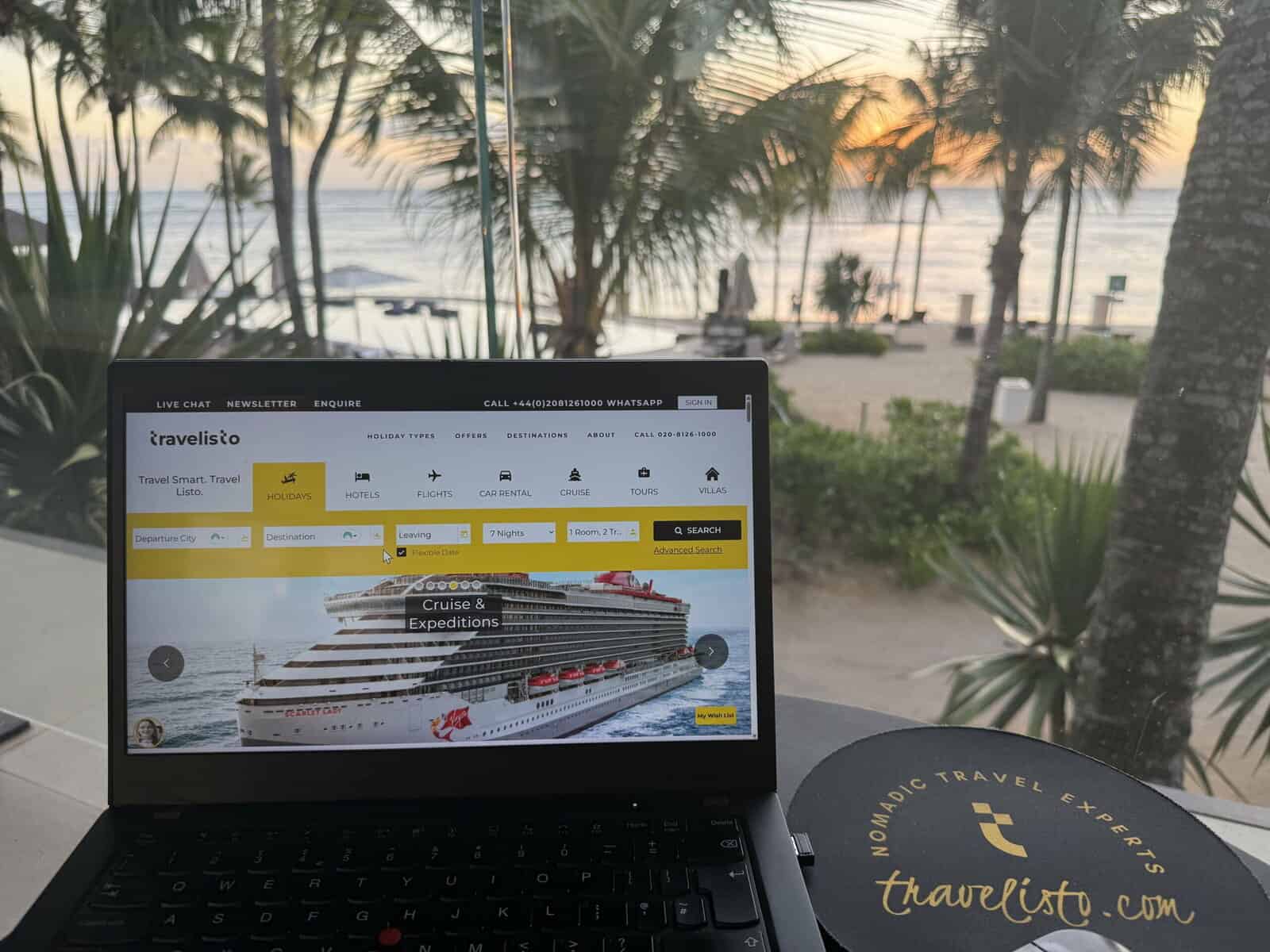 Laptop screen displaying travel booking website with cruise image, surfing sunset view with palm trees, beach and ocean in background