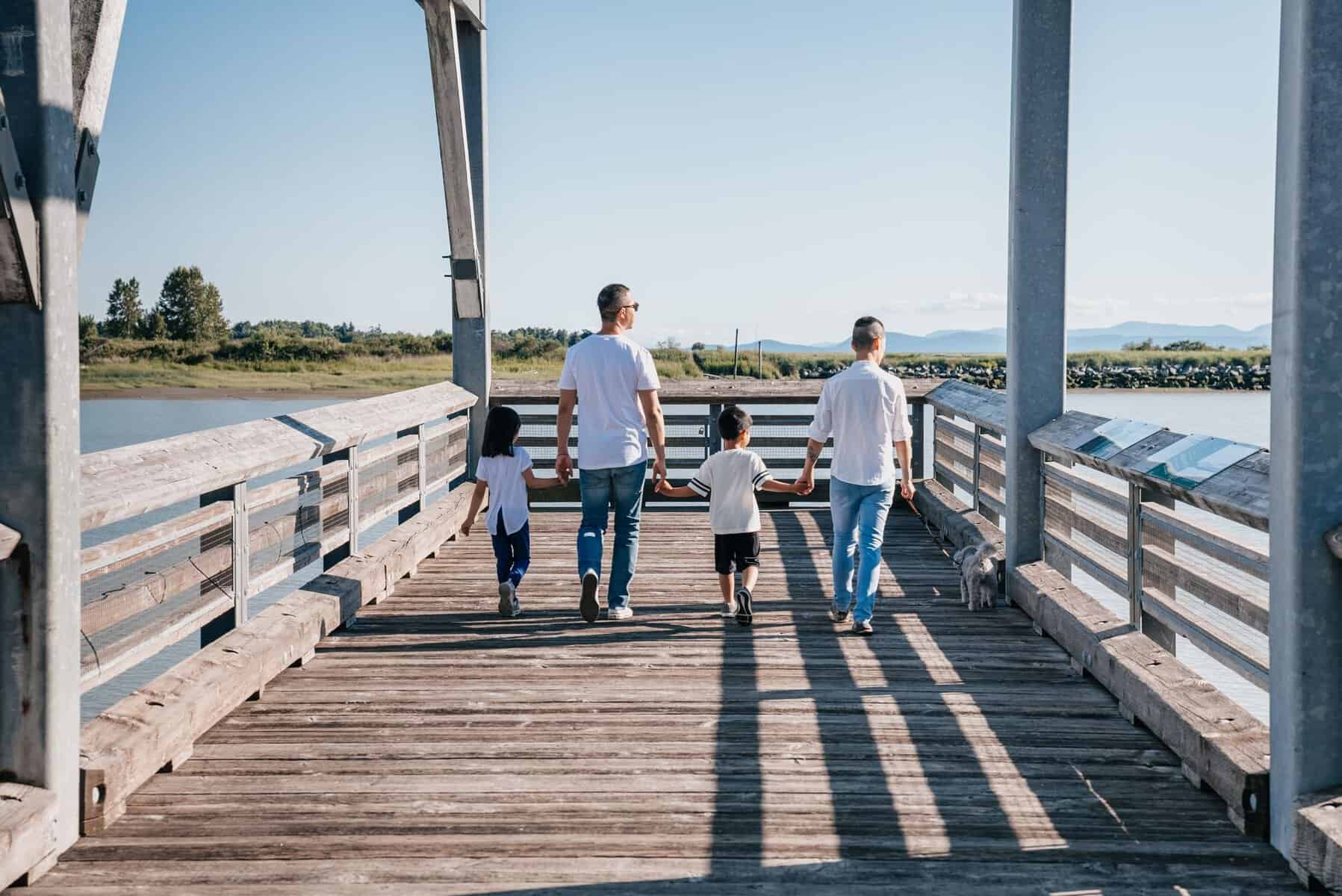 Two same-sex parents and children walk hand in hand on a sunny boardwalk
