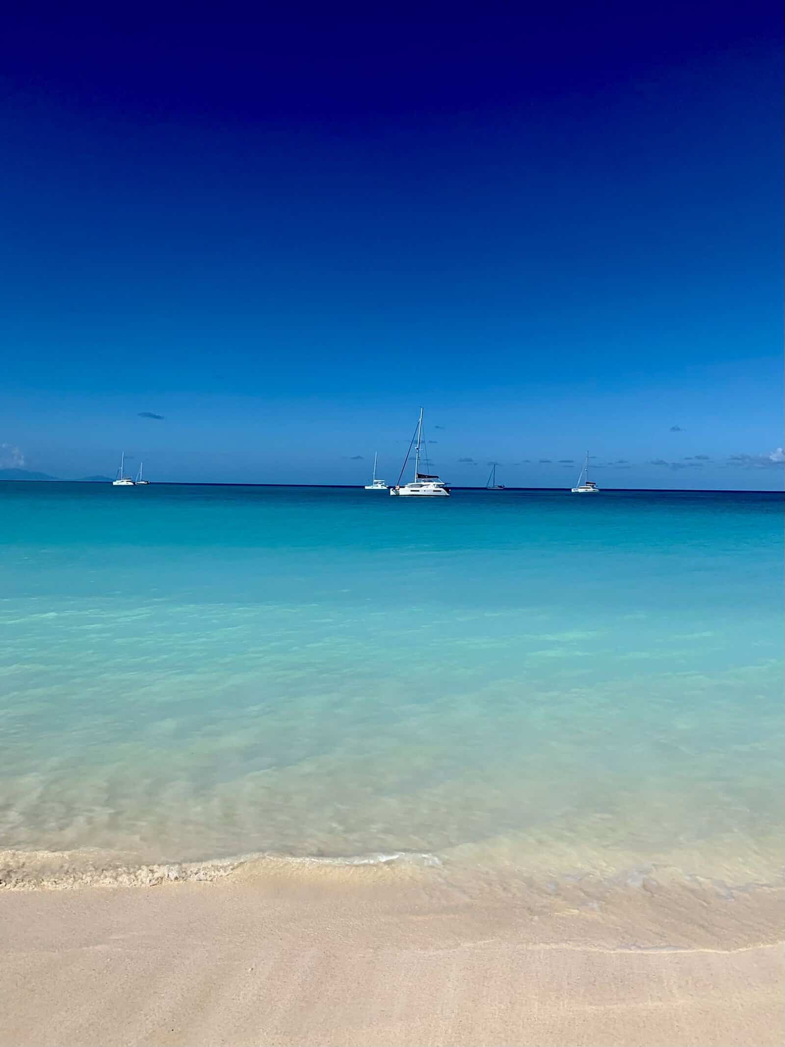 A calm beach with sailboats on the horizon in Antigua