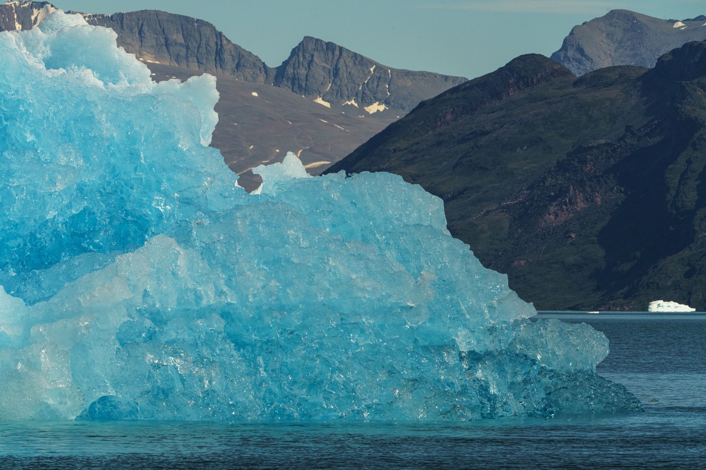A blue iceberg below rugged mountains