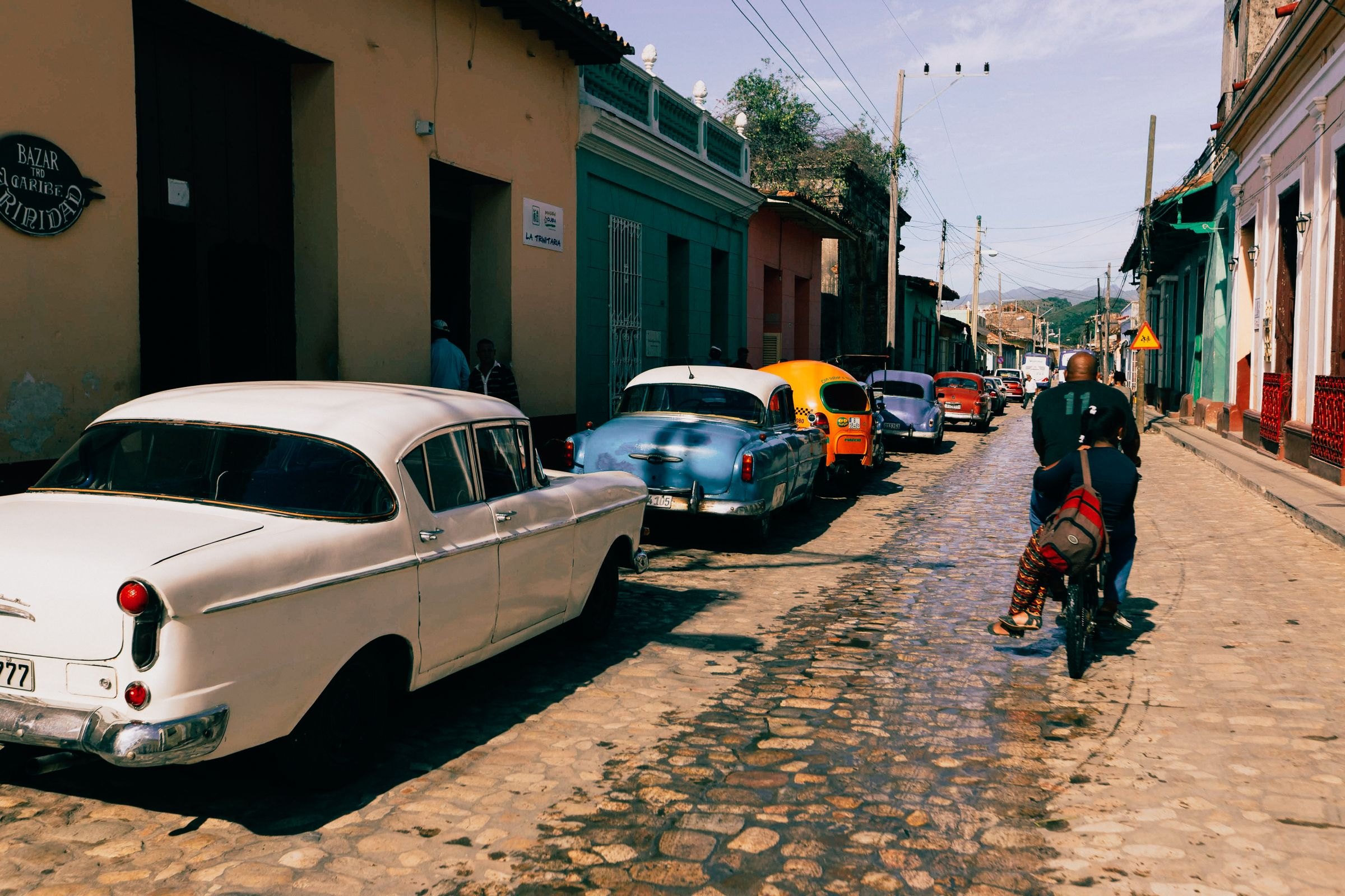 A cobbled Cuban street with classic cars and cyclists