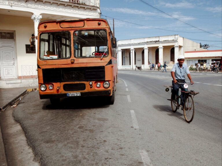 A cyclist passing a parked bus on a Cuban street
