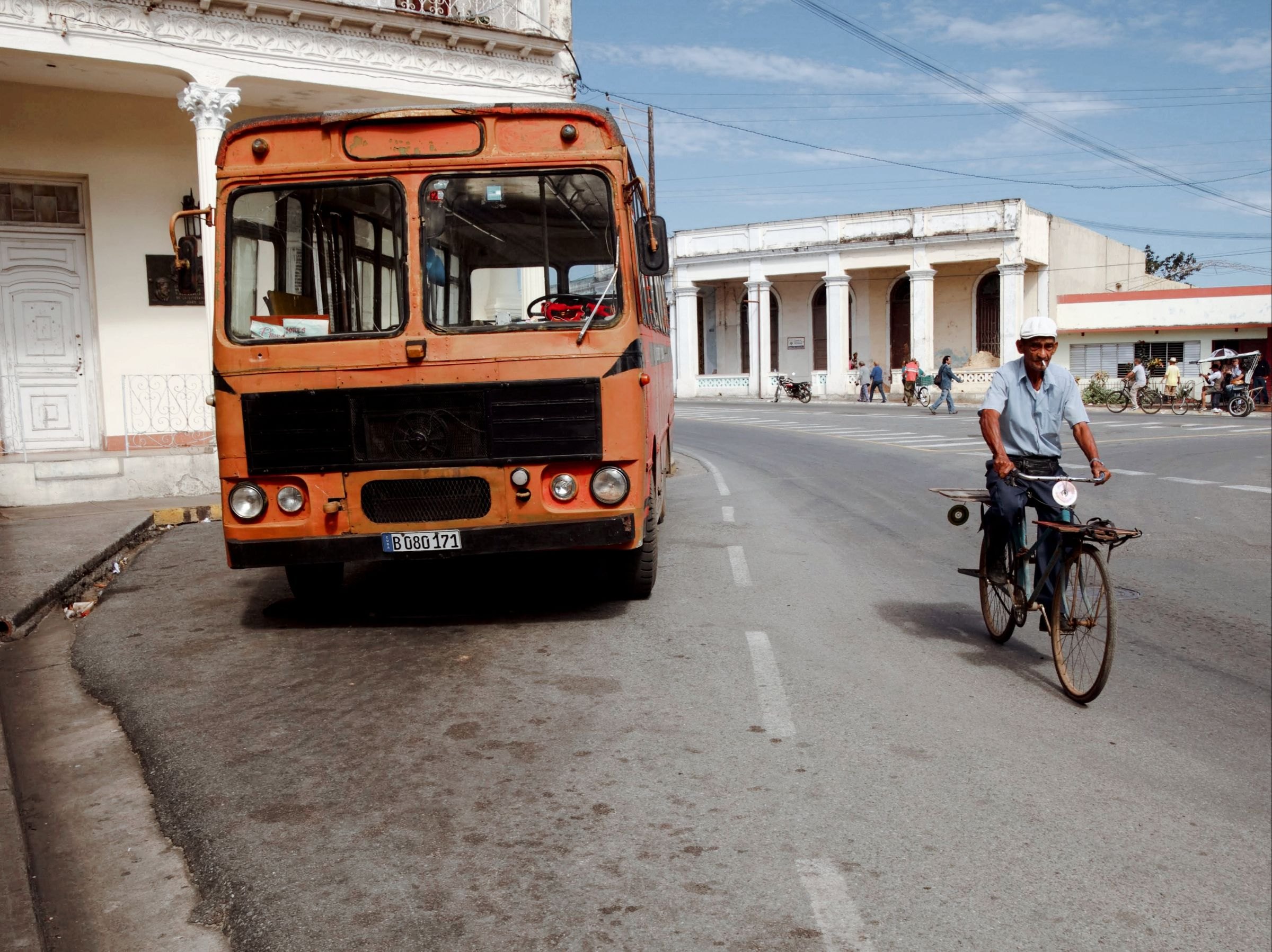 A cyclist passing a parked bus on a Cuban street