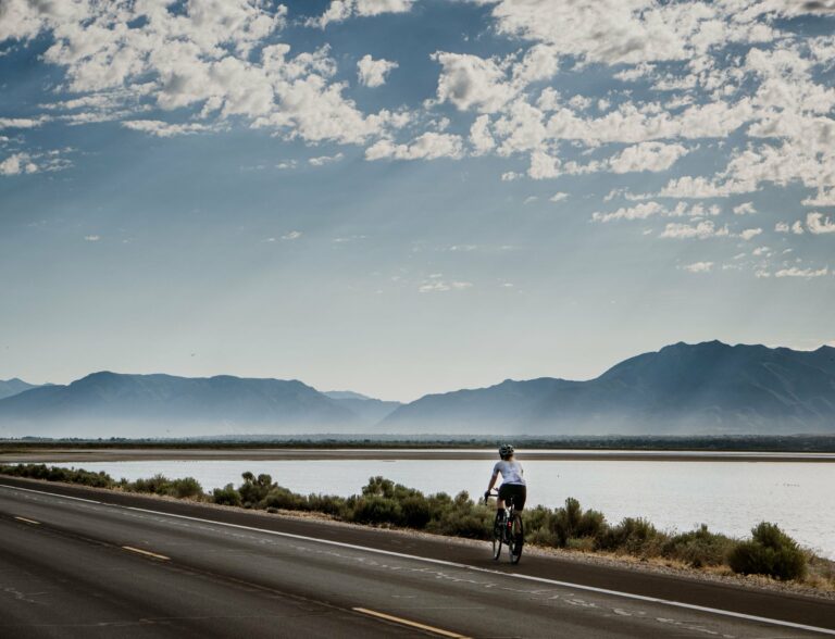 A cyclist on a lakeside road beneath mountains