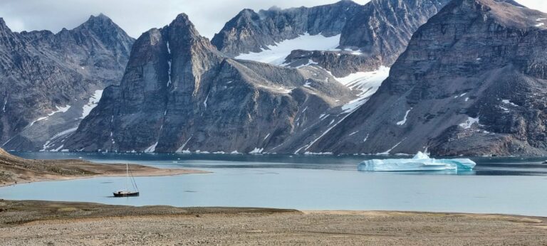 A Greenland fjord with an iceberg below jagged peaks