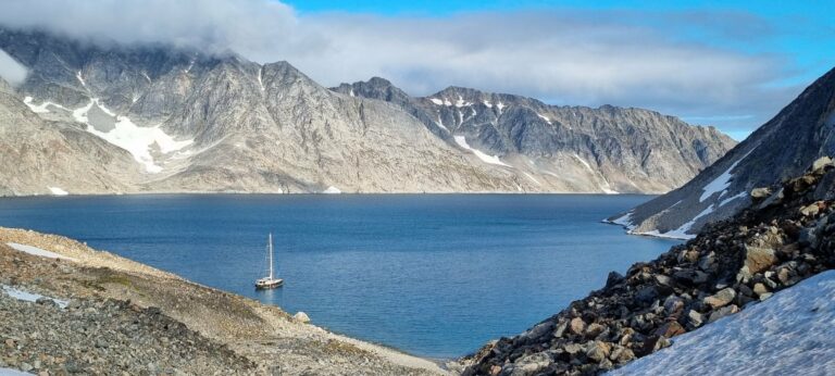 A sailing boat in a Greenland fjord below towering mountains