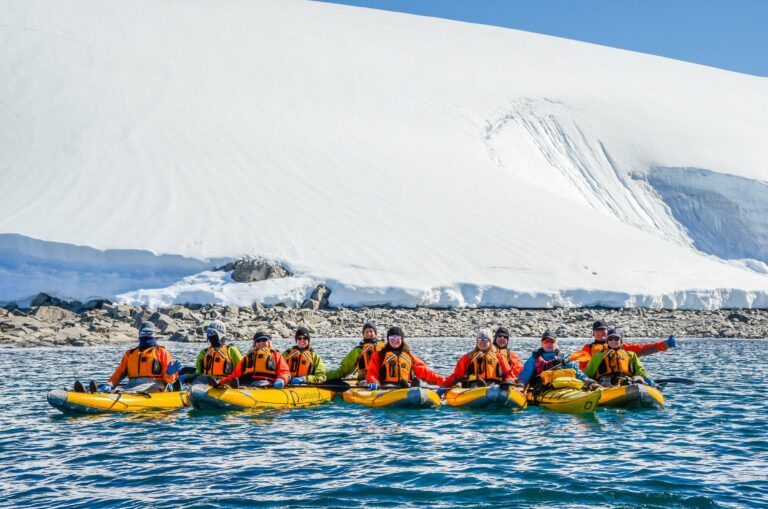 A group kayaking below an Antarctic ice cliff
