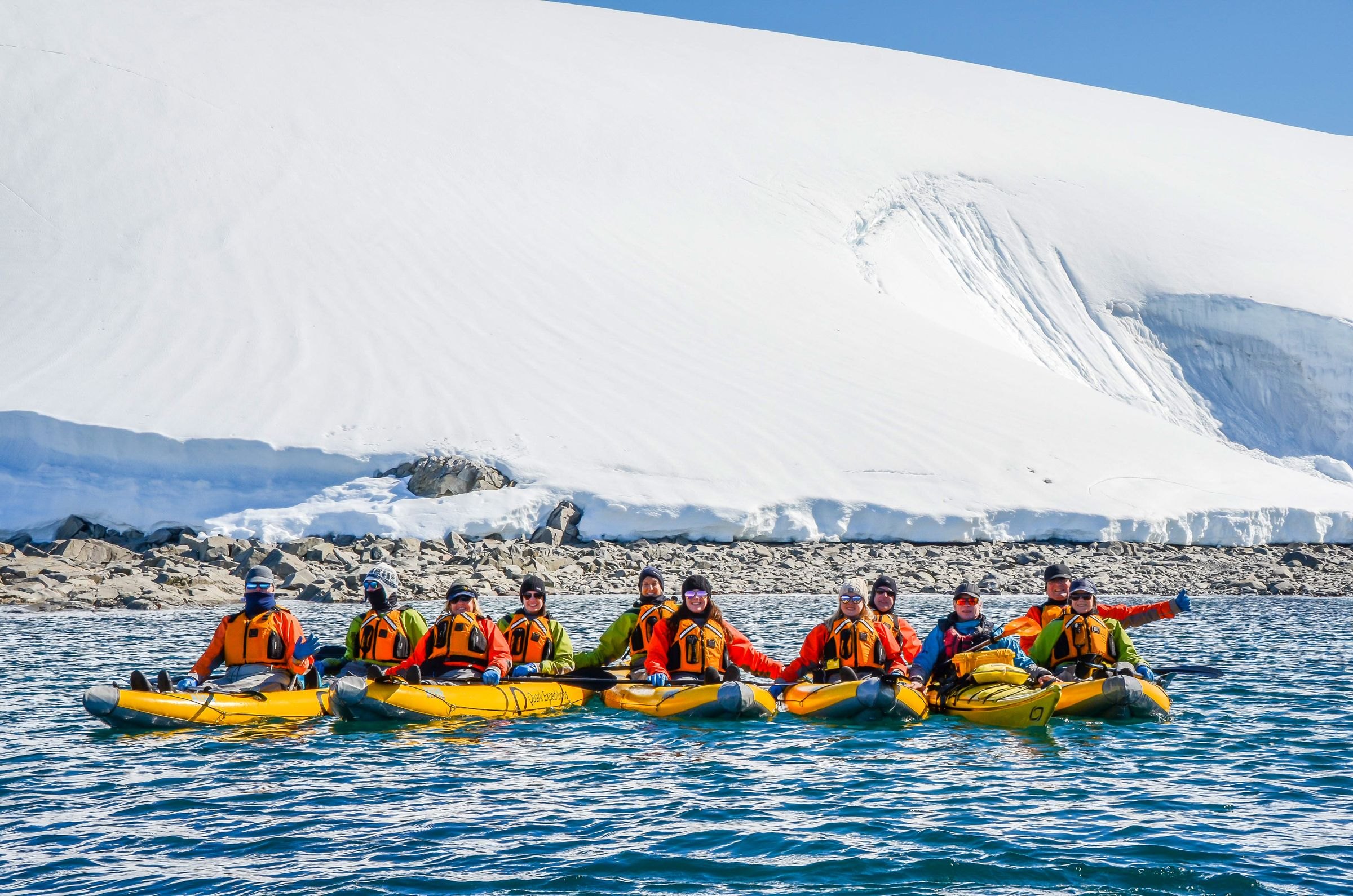 A group kayaking below an Antarctic ice cliff