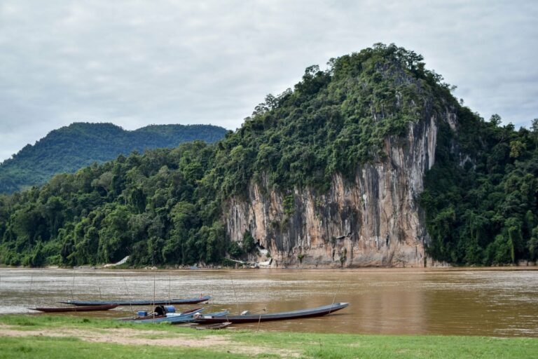 Longboats beneath forested cliffs in northern Laos