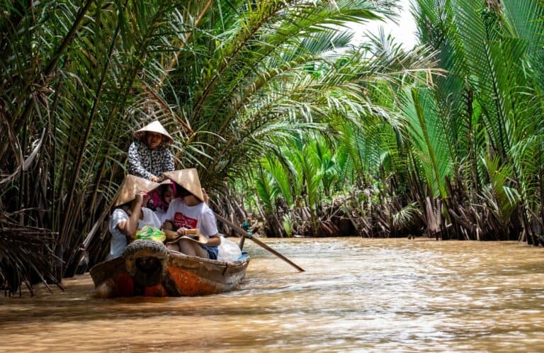 A traditional boat on a palm-lined channel of the Mekong Delta