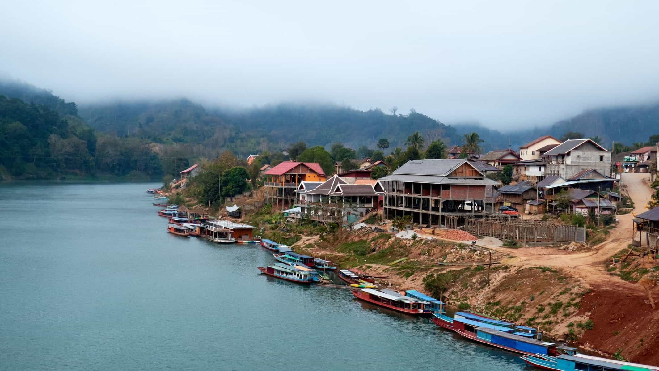Boats on a river beneath misty mountains in northern Laos