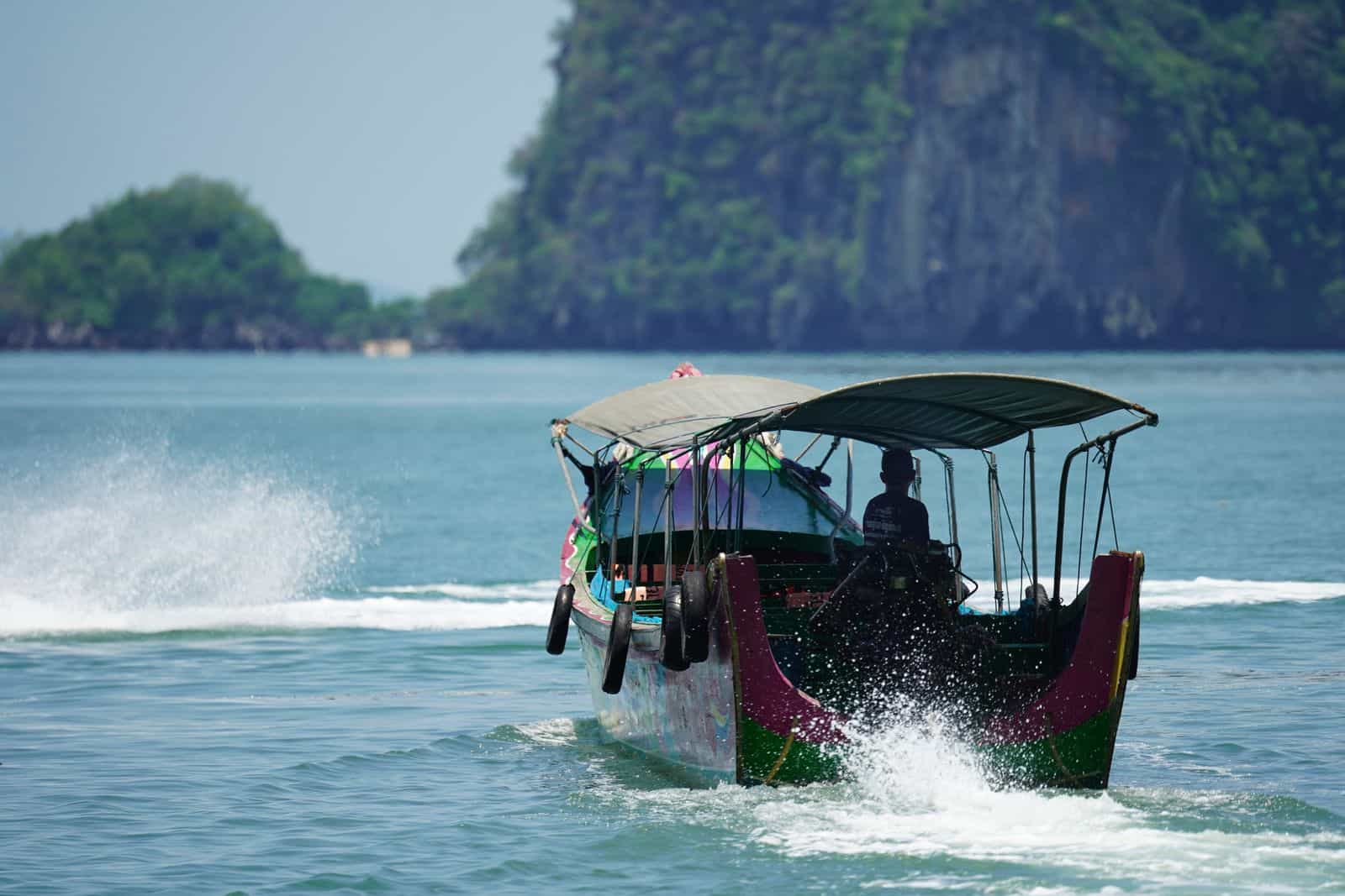 Traditional longtail boat with canopy cruising in a Thai tropical bay surrounded by green islands