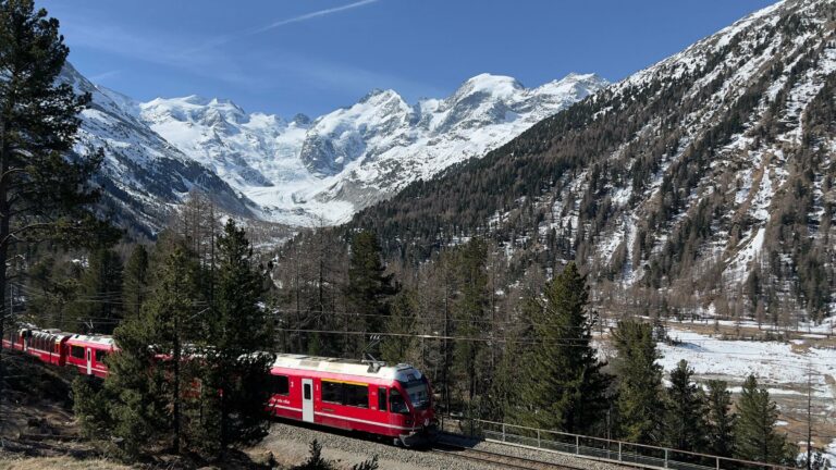 A red train passing through the snowy Alps