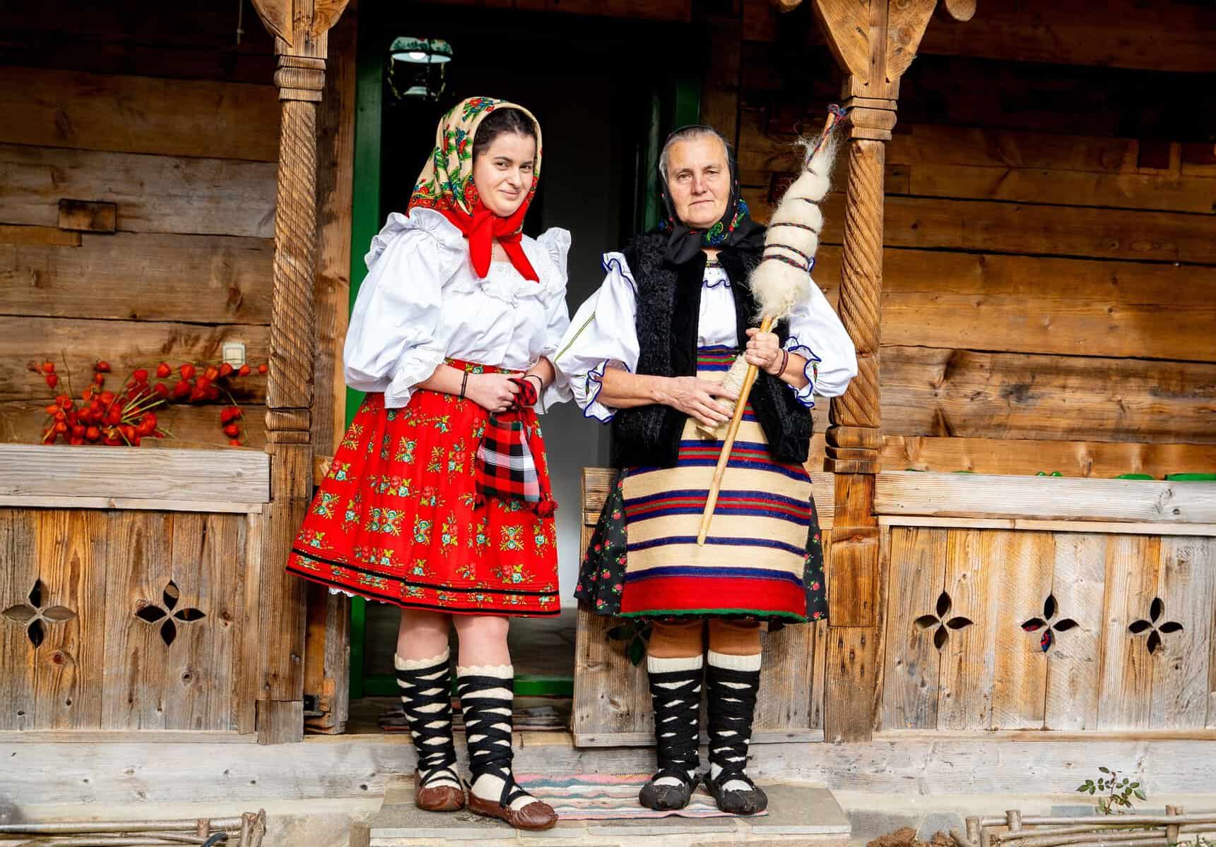 Two women in traditional Romanian folk costume on a wooden porch