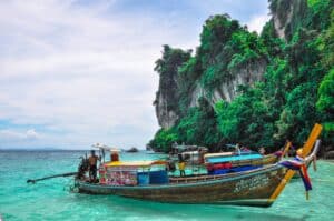 Longtail boat in turquoise water below limestone cliffs in southern Thailand
